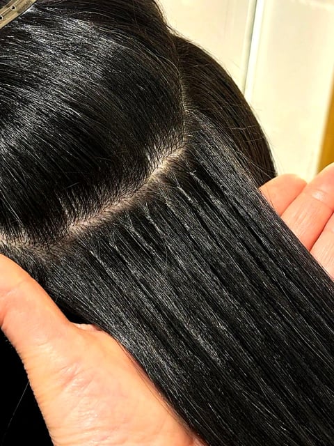Back view of a woman with long wavy platinum-blonde hair with a black bow, demonstrating the length and movement achievable with keratin bond extensions in London.